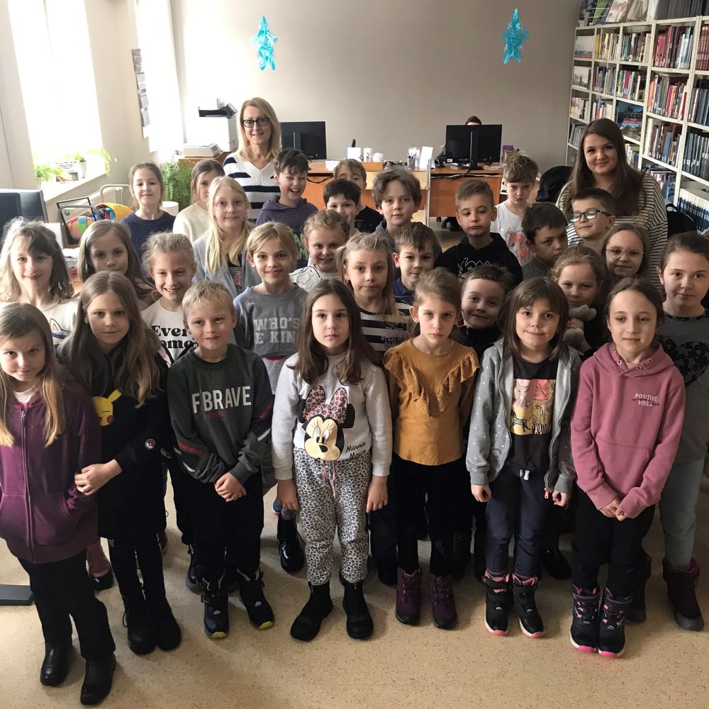 Grupa dzieci pozujących do zdjęcia w bibliotece.