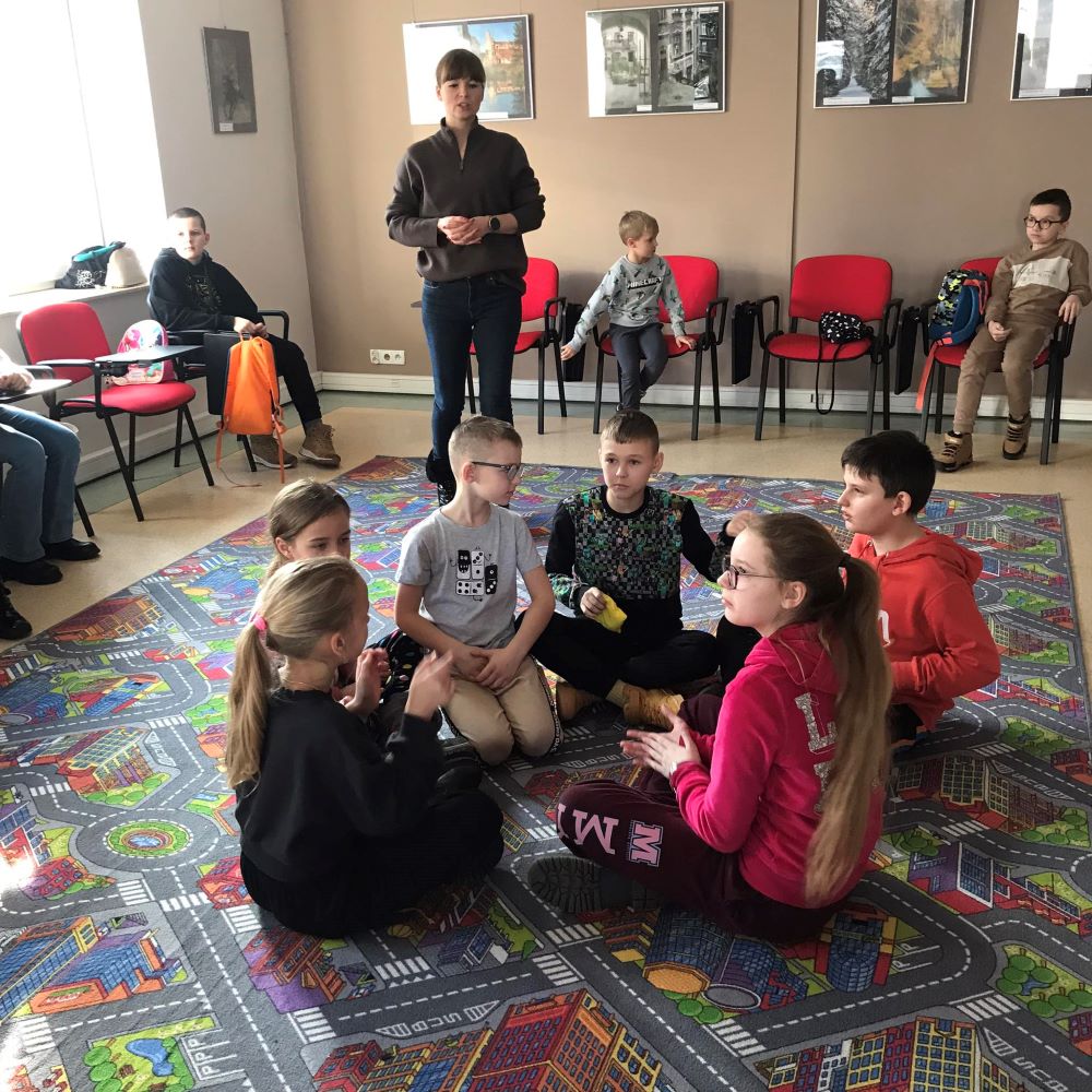 Grupa dzieci siedzi w kręgu na dywaniku.