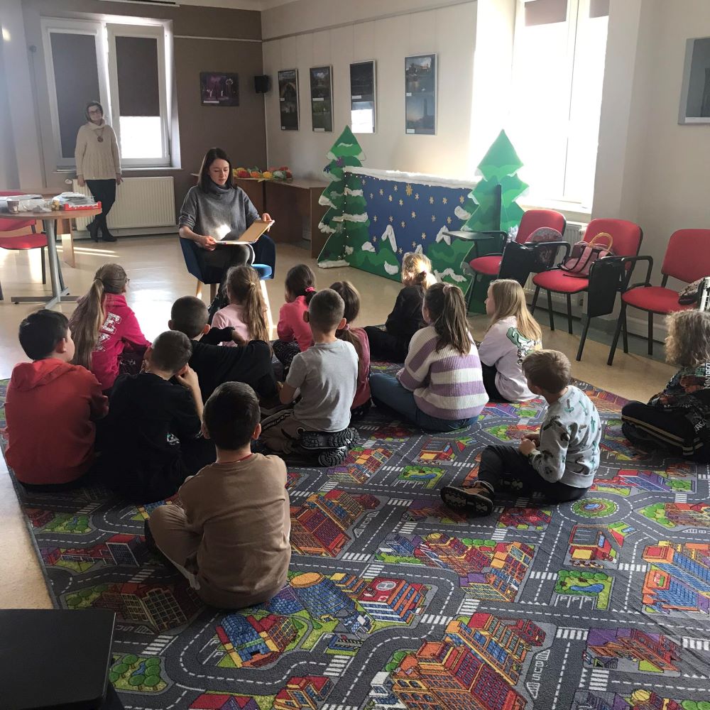 Grupa dzieci siedzi na podłodze przed choinką.