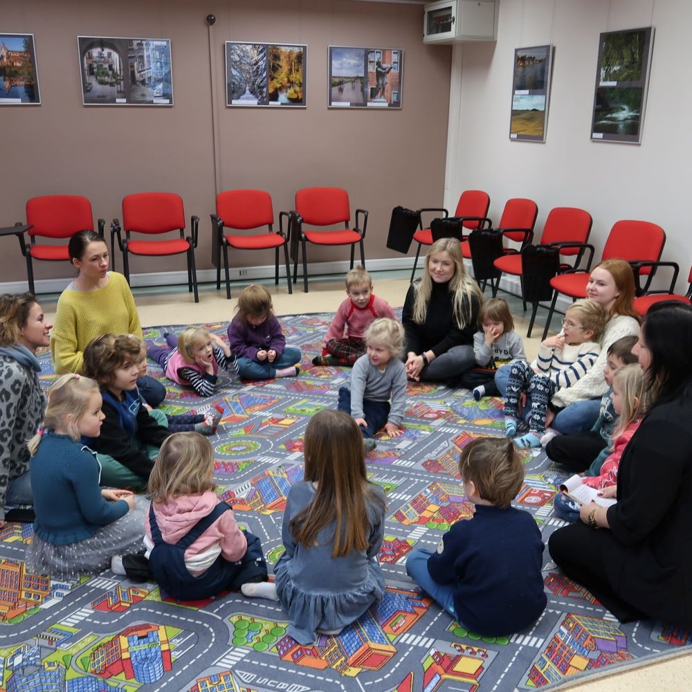 Grupa dzieci siedzących w kręgu na dywanie.