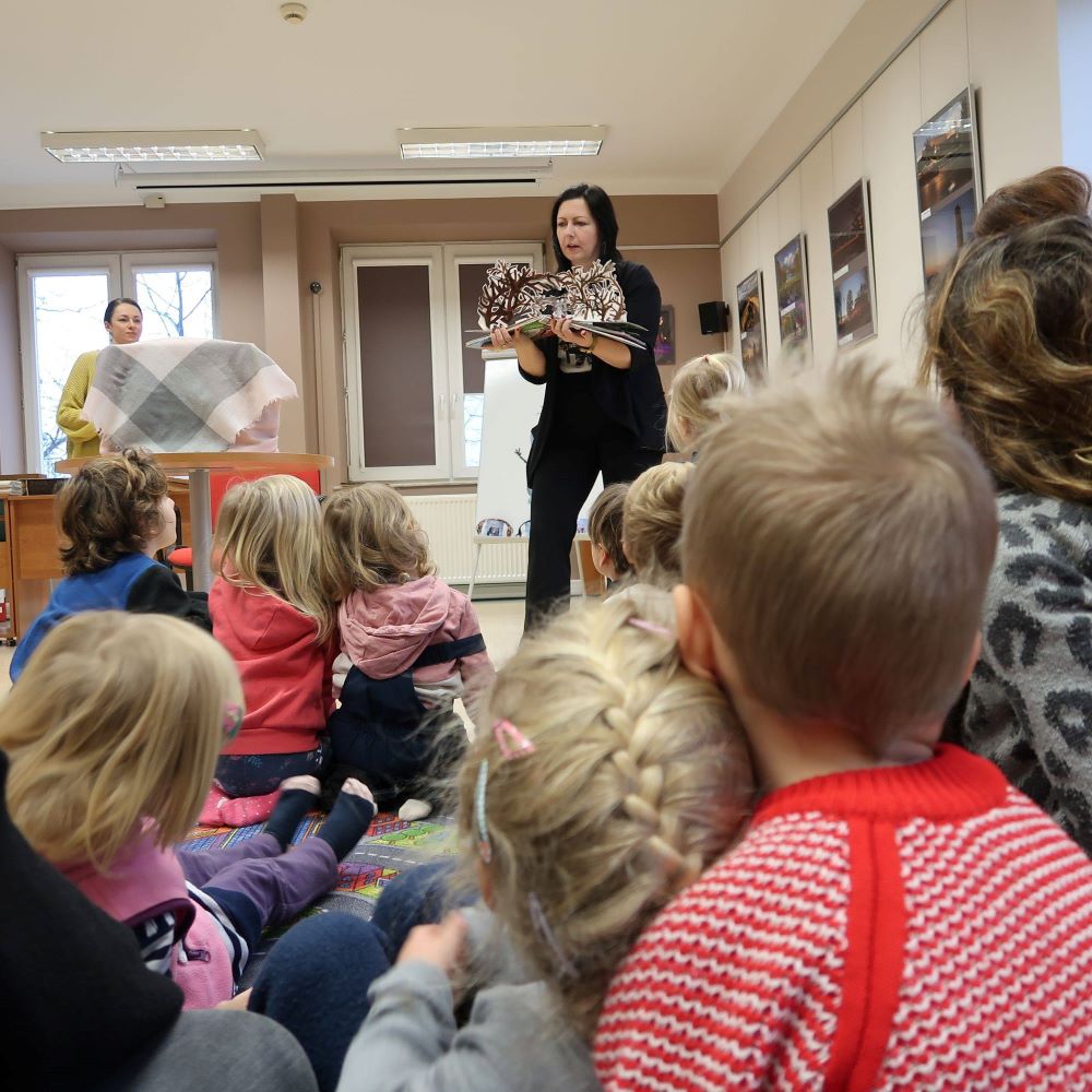 Kobieta czyta książkę grupie dzieci.