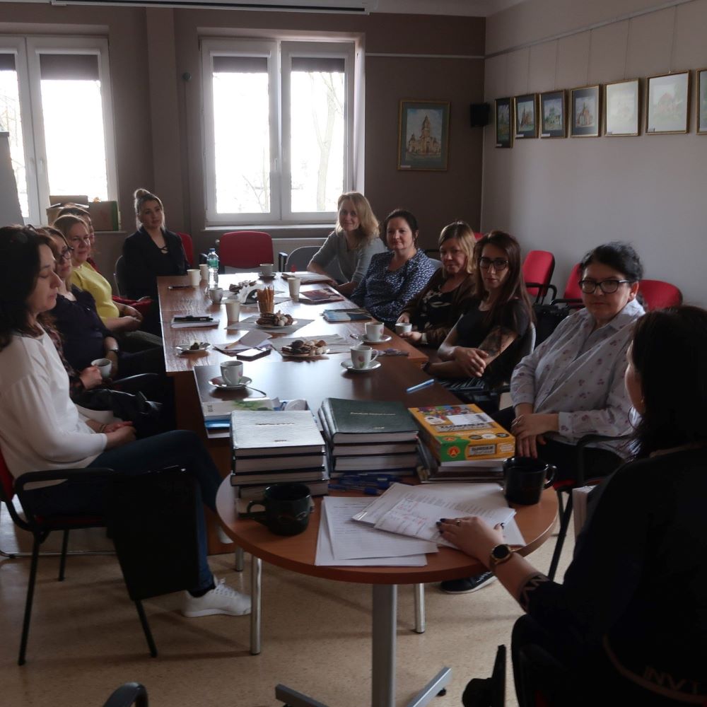 Grupa pań siedzących przy stole konferencyjnym uważnie słucha prelegentki.