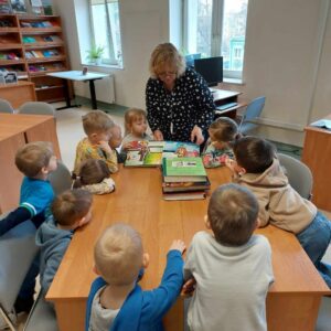 Grupa dzieci ogląda książki z obrazkami rozłożone na stole czytelnianym.