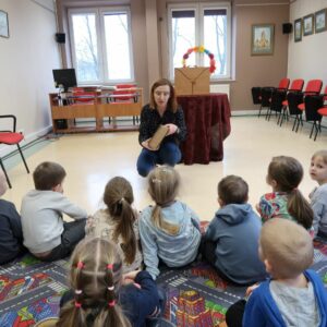 Dzieci siedzą na dywanie i oglądają najstarszą książkę drukowaną ze zbiorów biblioteki.