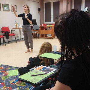 Kobieta stoi pośrodku sali i odgrywa scenę teatralną.