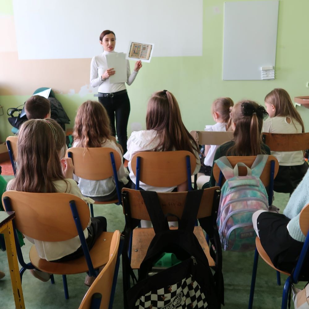 Pani bibliotekarka pokazuje dzieciom stronę książki pisanej ręcznie