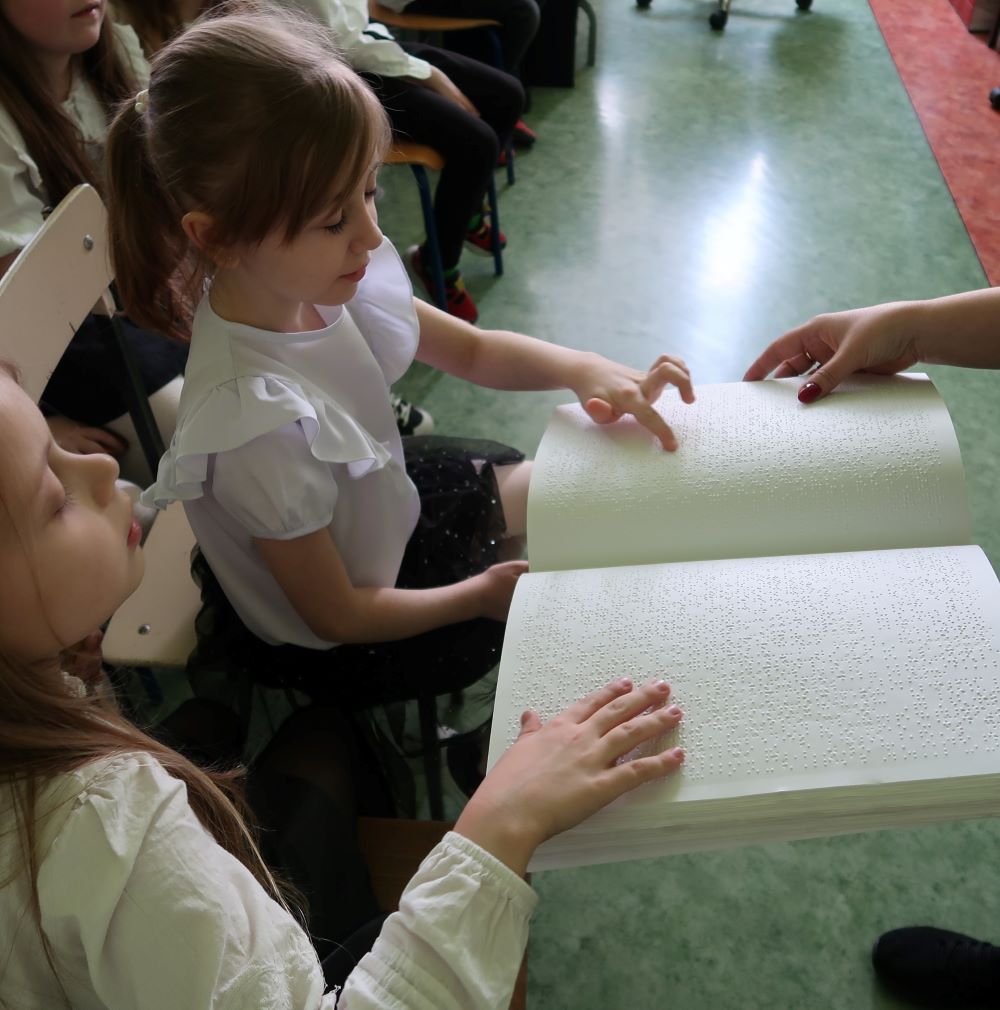 Dziewczynka wodzi palcem po kartce papieru zadrukowanej tekstem pisanym w alfabecie braila