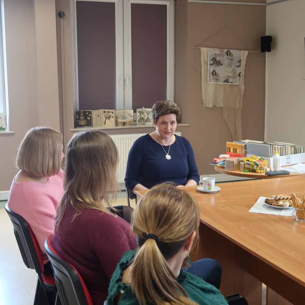 Grupa kobiet siedząc przy stole słucha z uwagą prowadzącej spotkanie