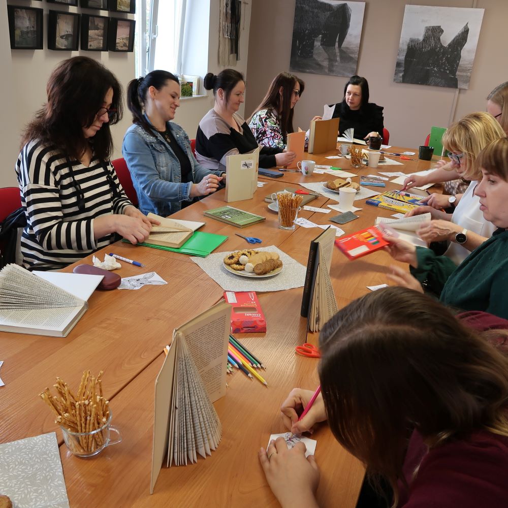 Grupa kobiet siedzących przy stole i tworzących ozdoby świąteczne ze starych książek