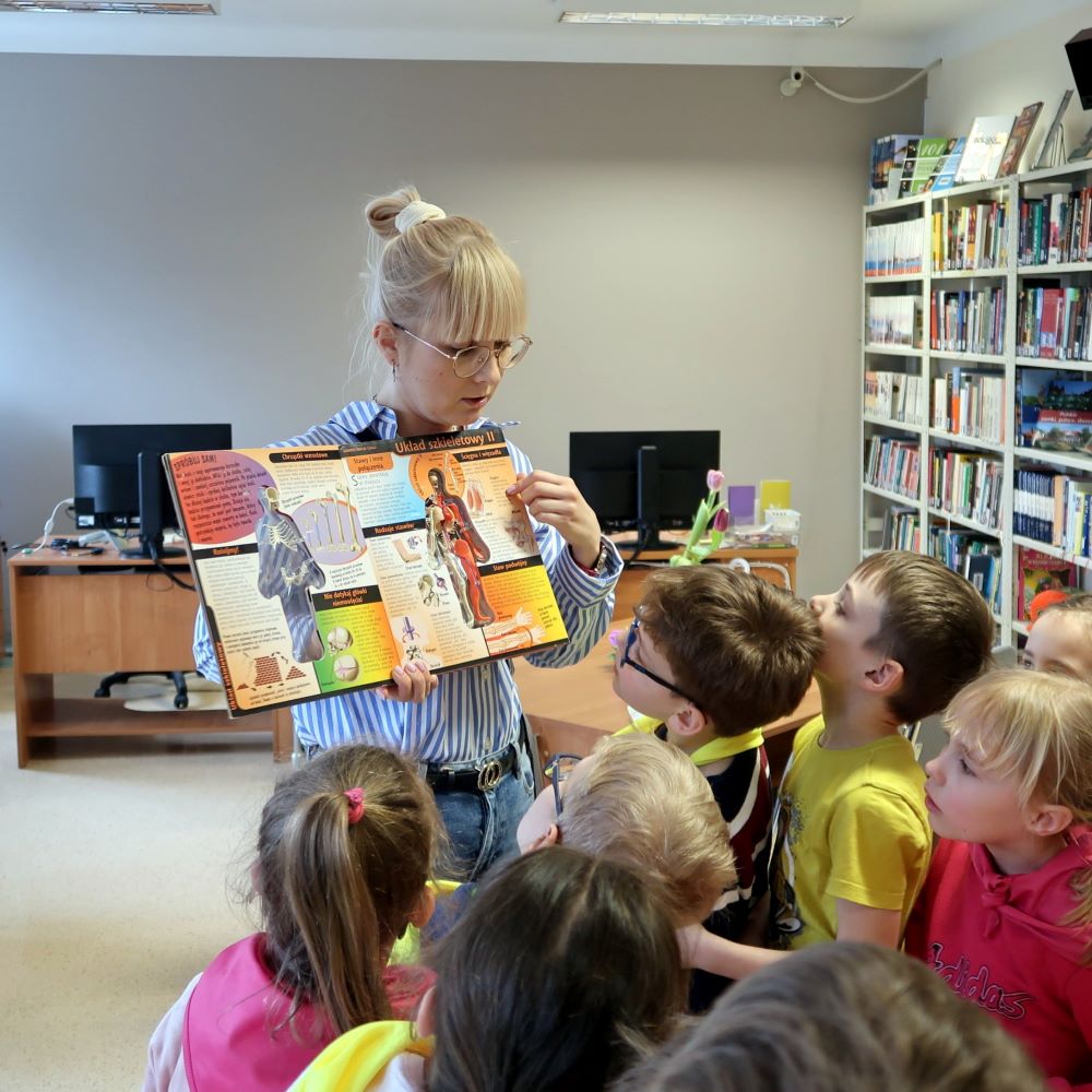 Bibliotekarka pokazuje dzieciom bogato ilustrowaną książkę.