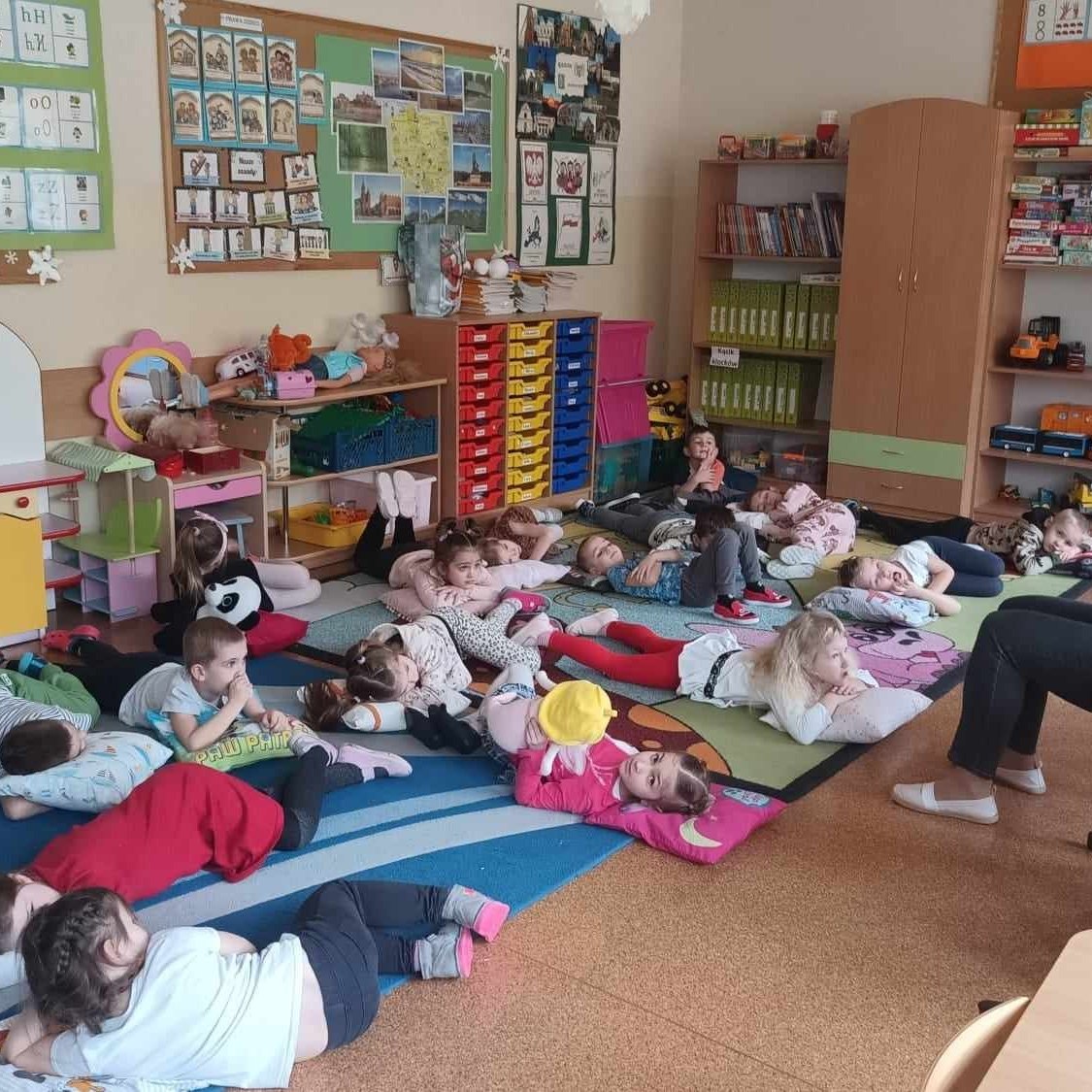 dzien-zaby-5 Dzieci leżąc na ziemi słuchają pani siedzącej na krześle