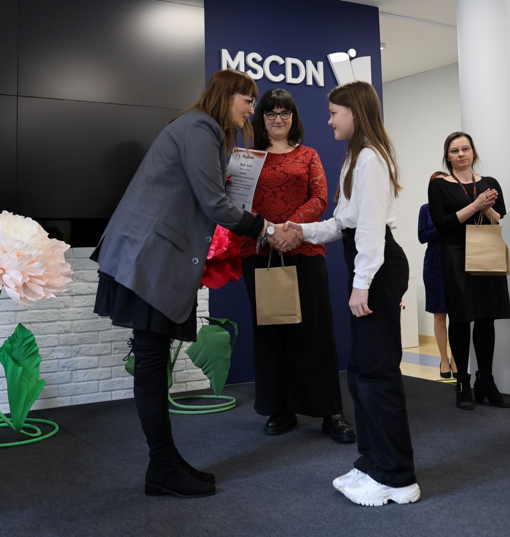 konkurs-tworczosc-literacka-4 Dwie członkinie jury wręczają nagrodę i dyplom młodej uczennicy