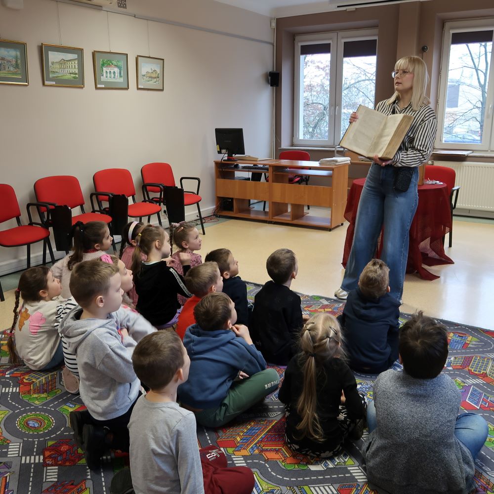 Pani bibliotekarka prezentuje dzieciom książkę czasopismo