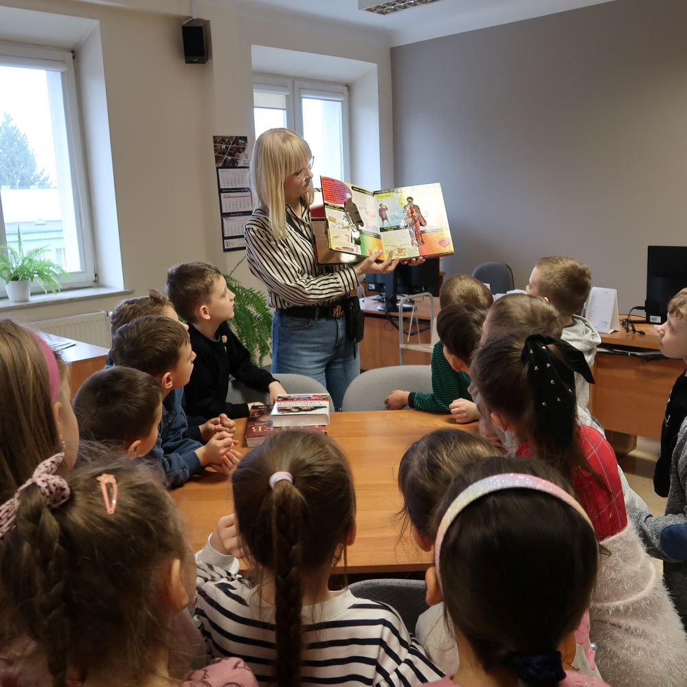 Pani bibliotekarka prezentuje dzieciom książkę obrazkową.