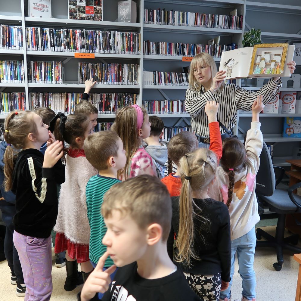 Pani bibliotekarka prezentuje dzieciom książkę obrazkową.