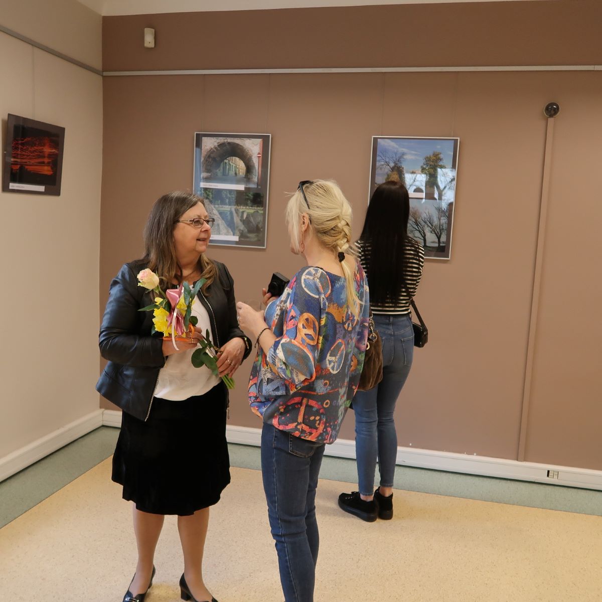 Kobieta z kwiatem w dłoni rozmawia w dziennikarką podczas wernisażu