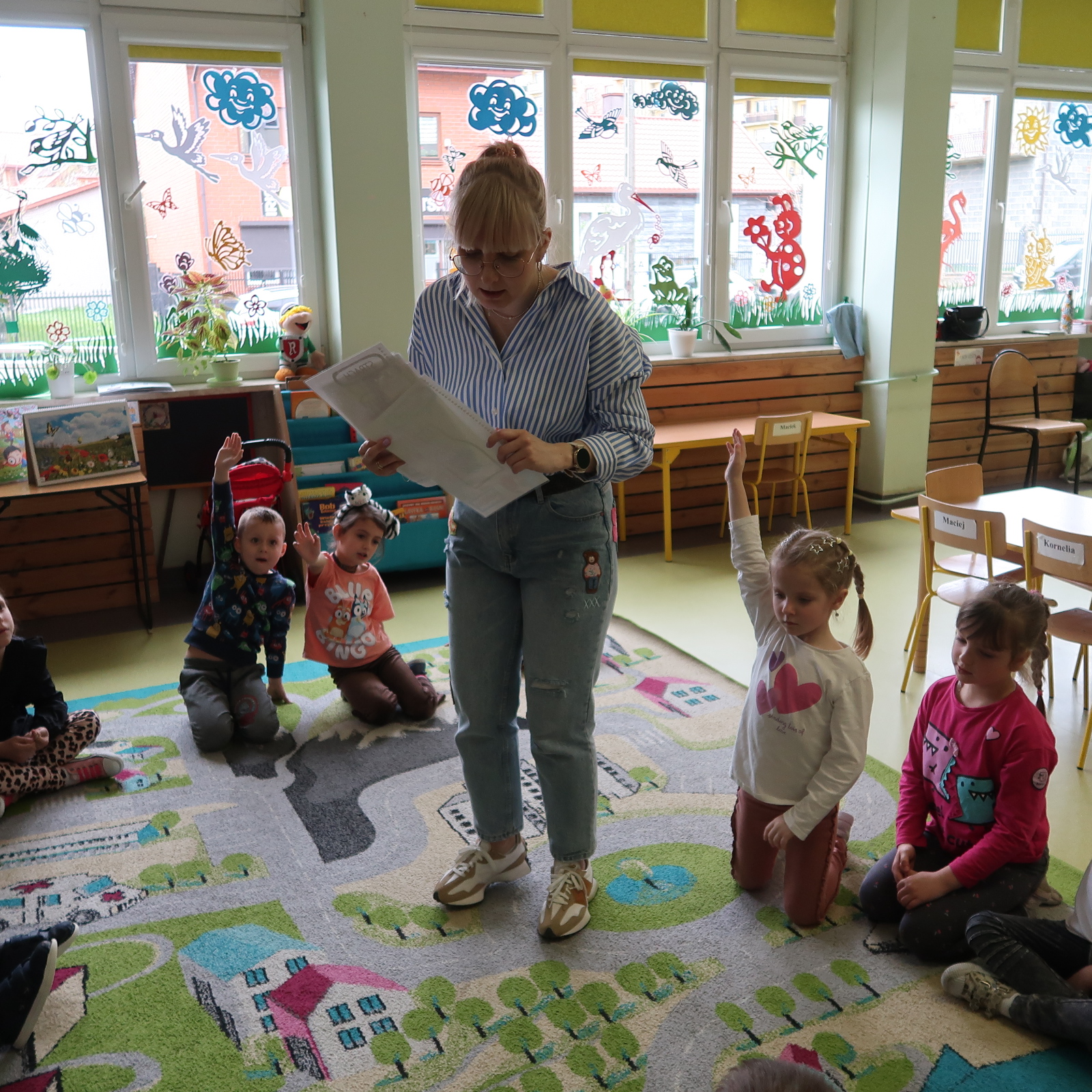 Bibliotekarka rozdaje dzieciom kartki ilustrujące różne emocje