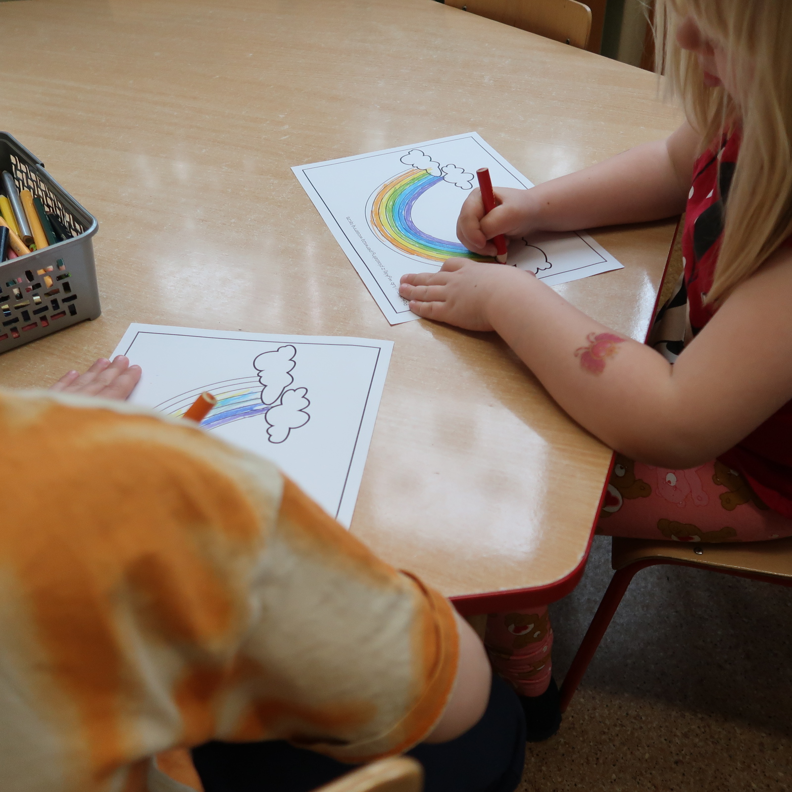 Dzieci kolorują rysunki tęczy na kartkach papieru.
