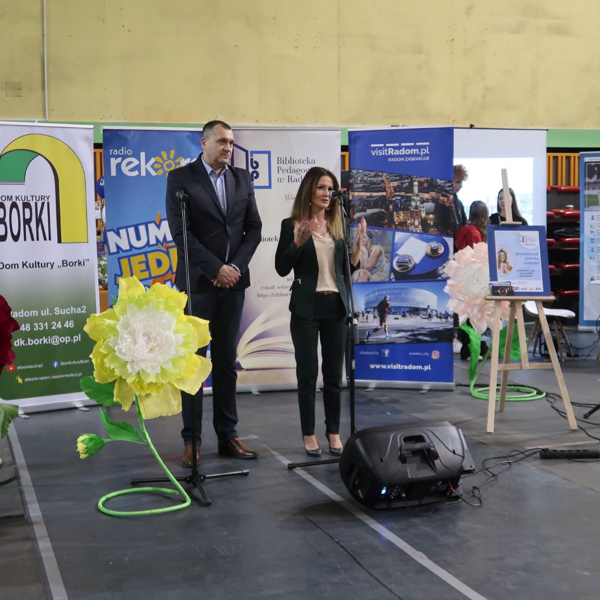 Kobieta i mężczyzna stoją przy mikrofonie w tle oferta edukacyjna radomskich szkół