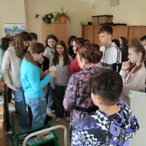 rozGRYzc-biblioteke-2 Uczennica odczytuje zapisaną na kartce papieru zagadkę do rozwiązania pozostali uważnie słuchają