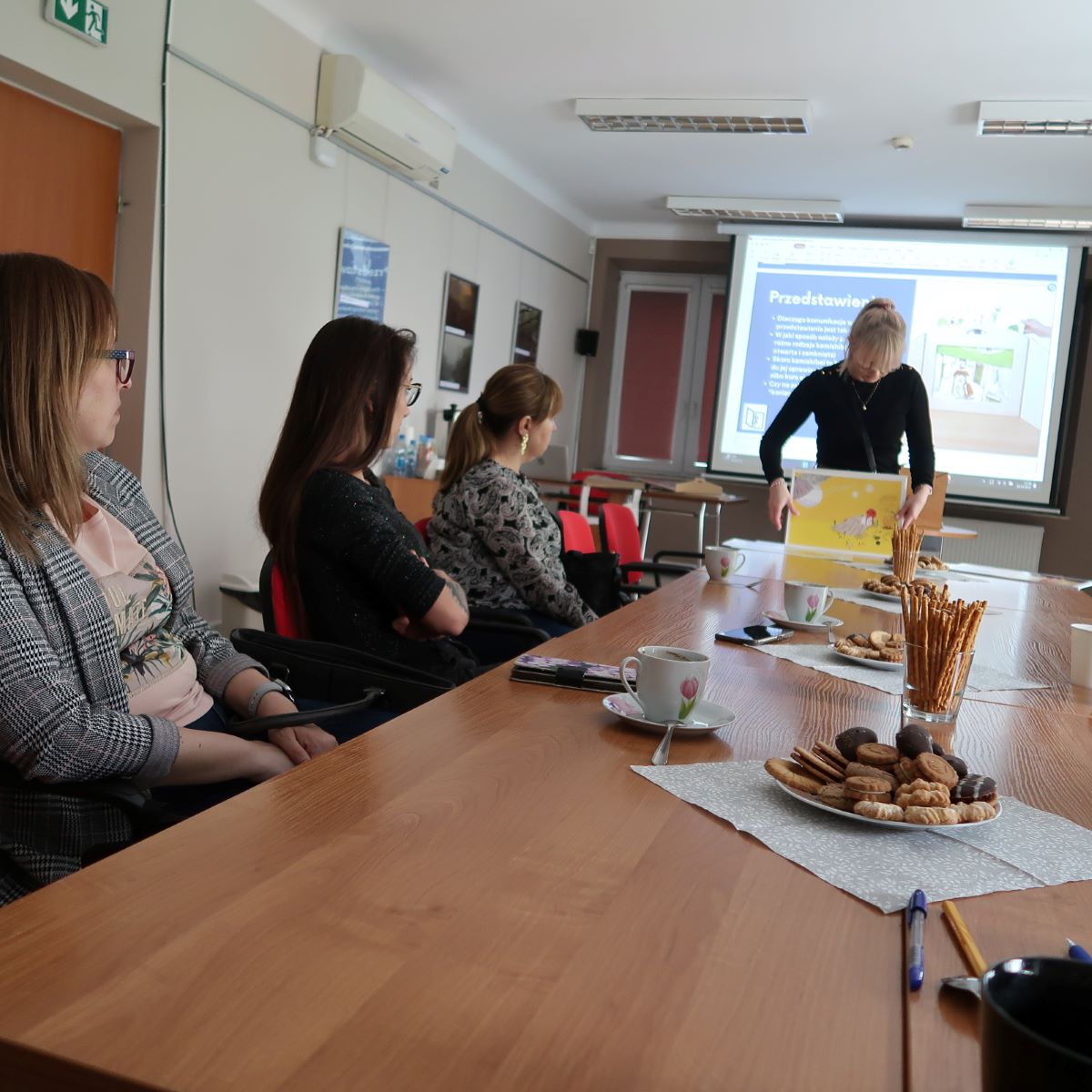 Grupa osób siedzi przy stole i słucha z uwagą prelegenta