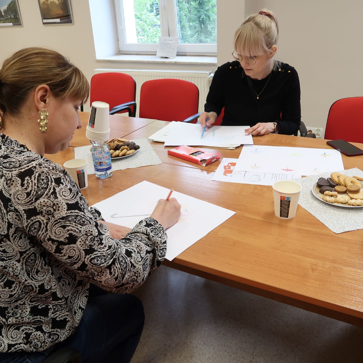 Grupa osób siedzi przy stole słuchając prelegenta