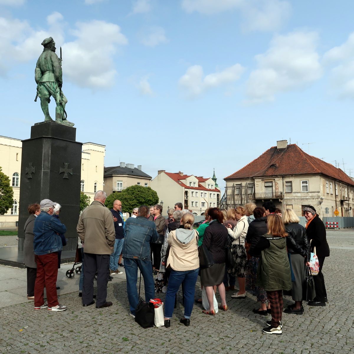 zwiedzanie-radomia-2 Grupa ludzi w różnym wieku zebranych wokół przewodnika w tle pomnik legionisty