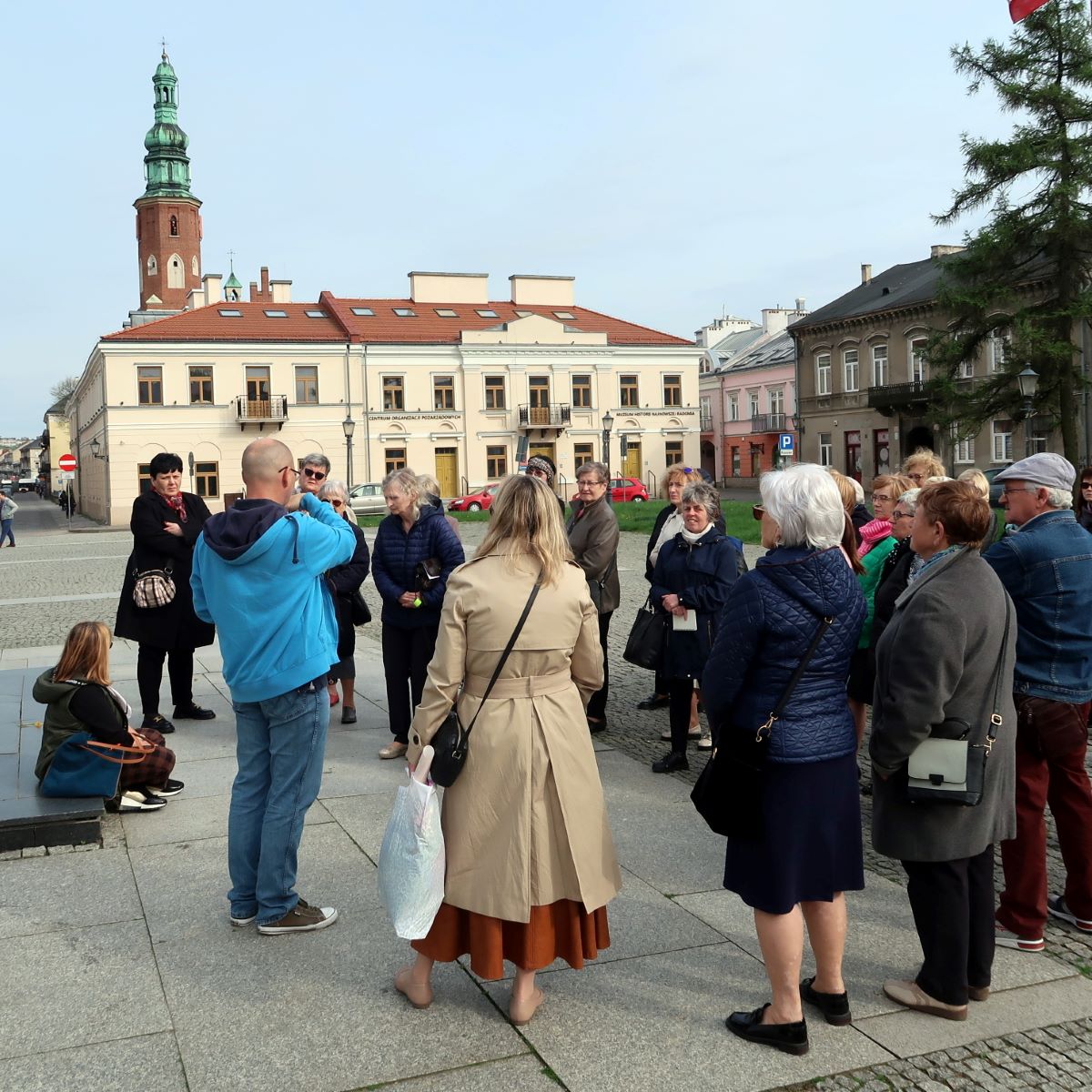 zwiedzanie-radomia-3 Grupa ludzi w różnym wieku zebranych wokół przewodnika w tle zabytkowe kamieniczki