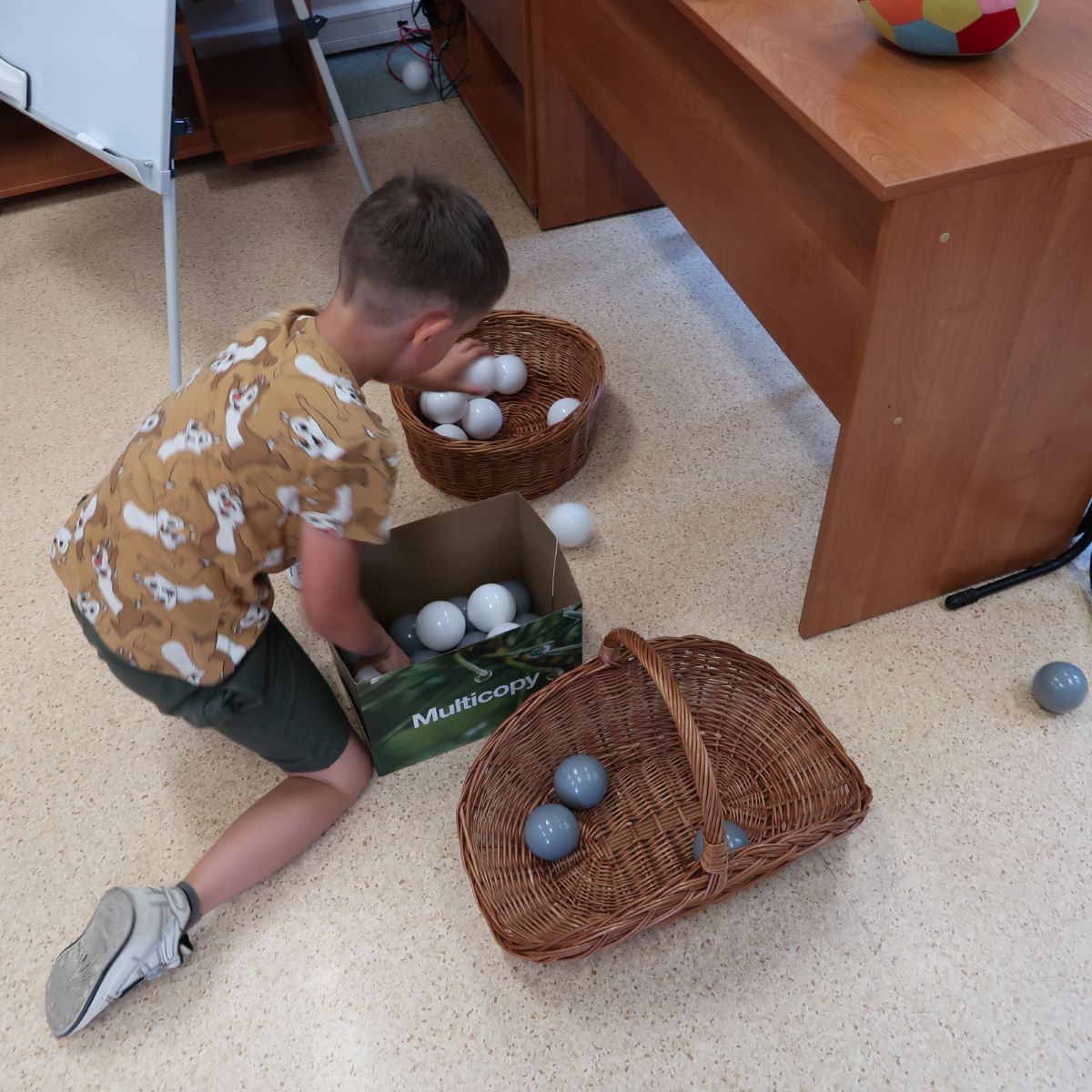 Chłopiec przekłada białe piłeczki z pudełka do koszyczka