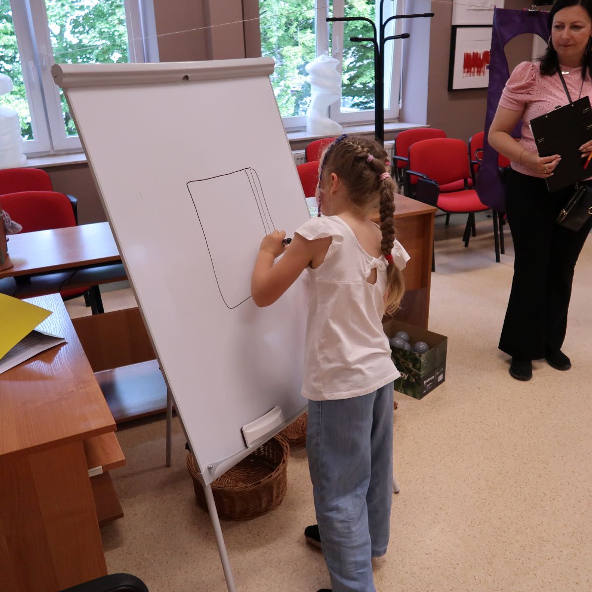 Dziewczynka rysuje na dużej kartce papieru zawieszonej na tablicy