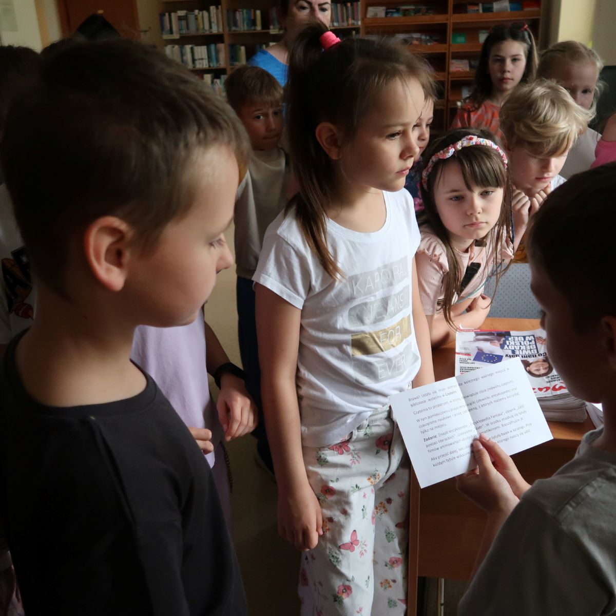 akademia-ksiazki-psp24-2 Jedno z dzieci odczytuje tekst zapisany na kartce papieru, pozostałe dzieci uważnie słuchają