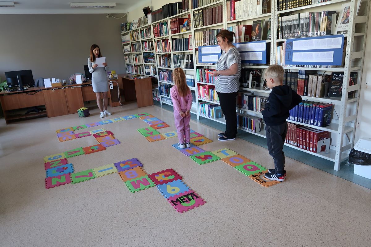 Mała dziewczynka porusza się po kwadratach z narysowanymi literami, które są rozłożone na podłodze