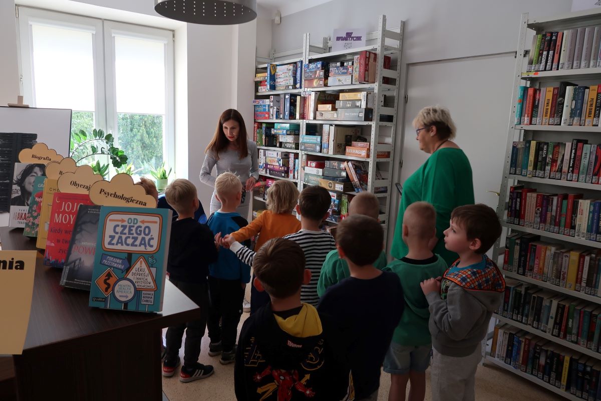 Dzieci oglądają zgromadzone na półkach bibliotecznych zbiory