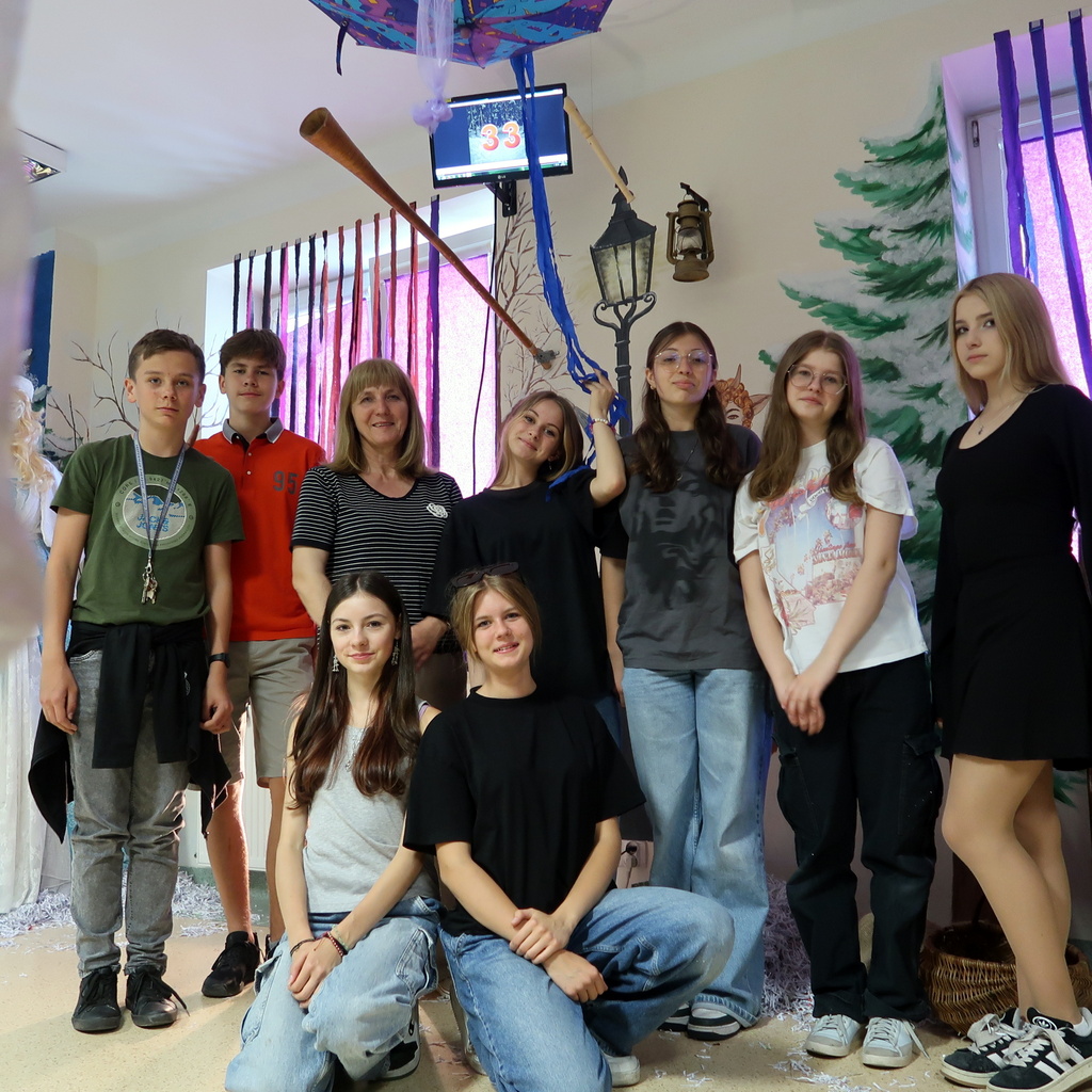 Grupa dziewięciu osób, w tym dorośli i nastolatki, pozuje do zdjęcia w udekorowanym pokoju.