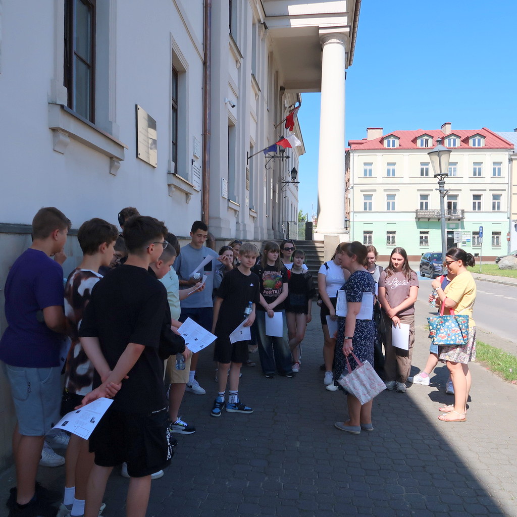 Grupa nastolatków gromadzi się przed wejściem do jasnego budynku z wysokimi kolumnami.