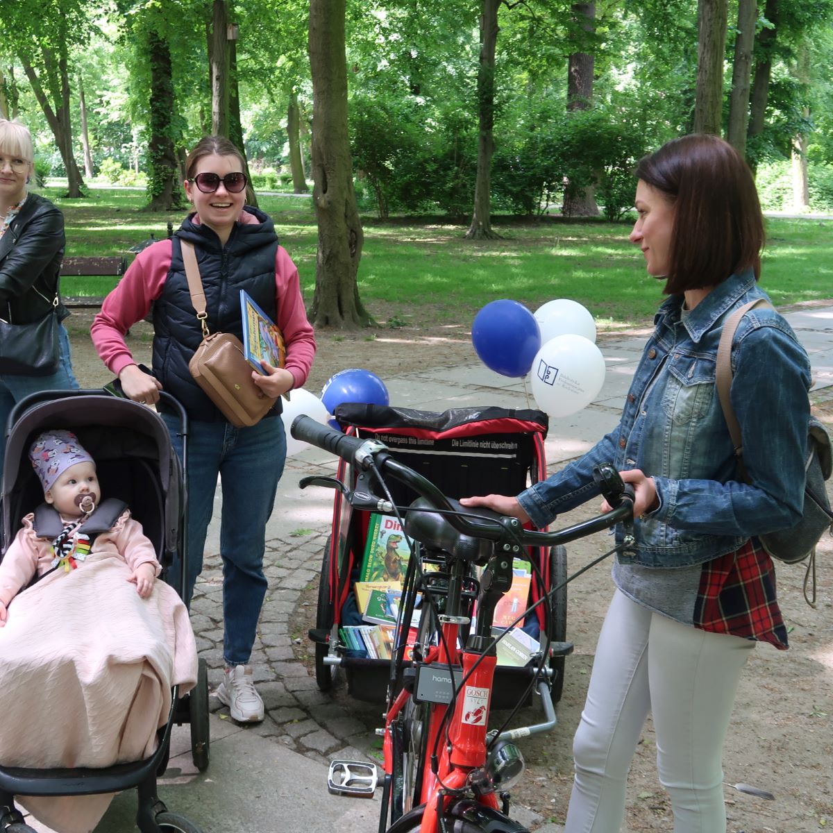 Młoda kobieta z dzieckiem w wózku zatrzymuje się przed wózkiem rowerowym zapakowanym książkami
