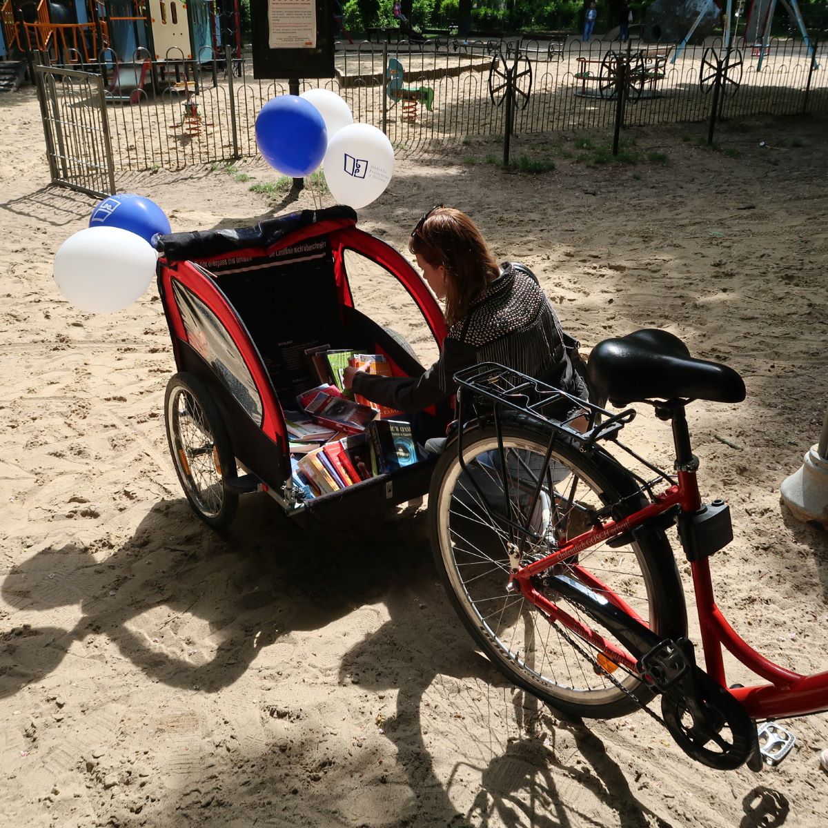 Młoda kobieta przegląda książki umieszczone w wózku rowerowym