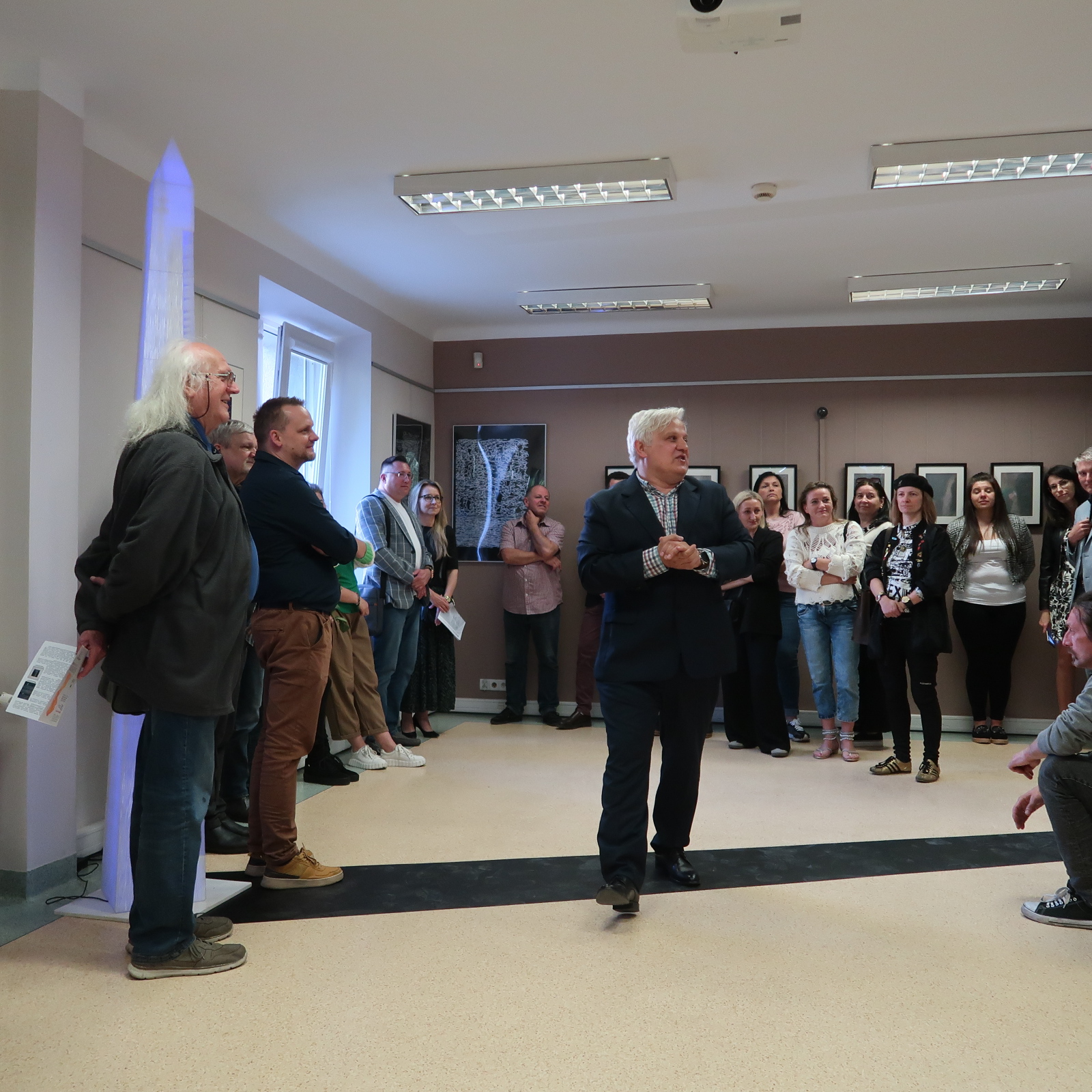 wystawa-noga-6 Starszy elegancki pan stojąc na środku sali wystawowej przemawia do zgromadzonych