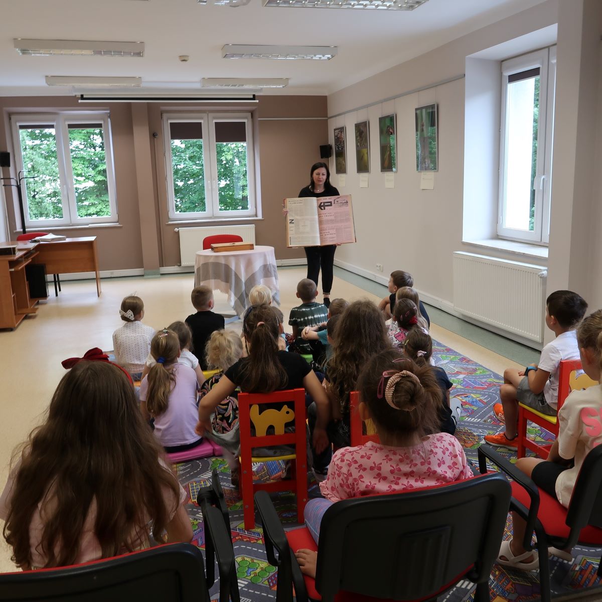 Młoda kobieta pokazuje dzieciom rozłożoną książkę.