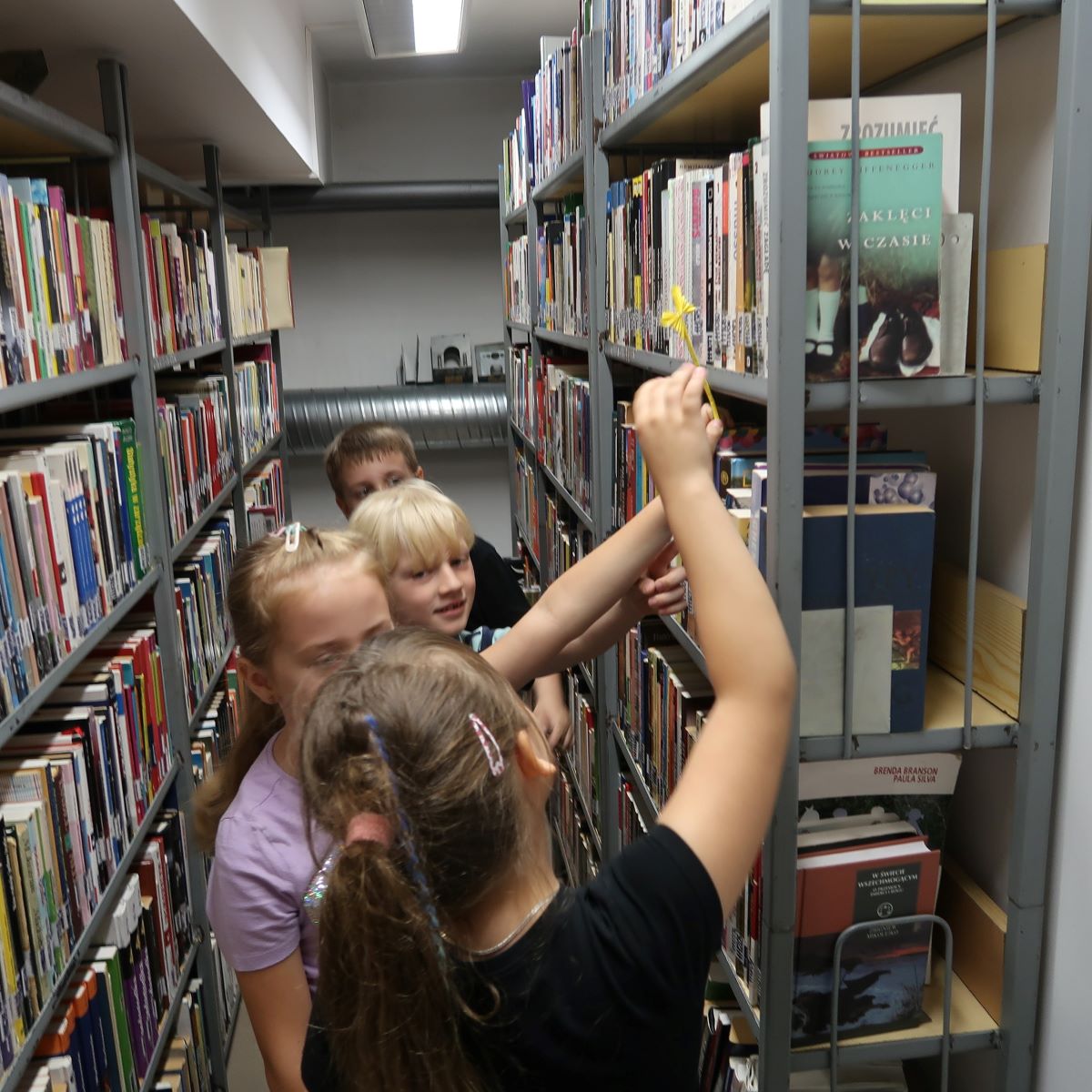 Grupa dzieci stoi przed regałem z książkami