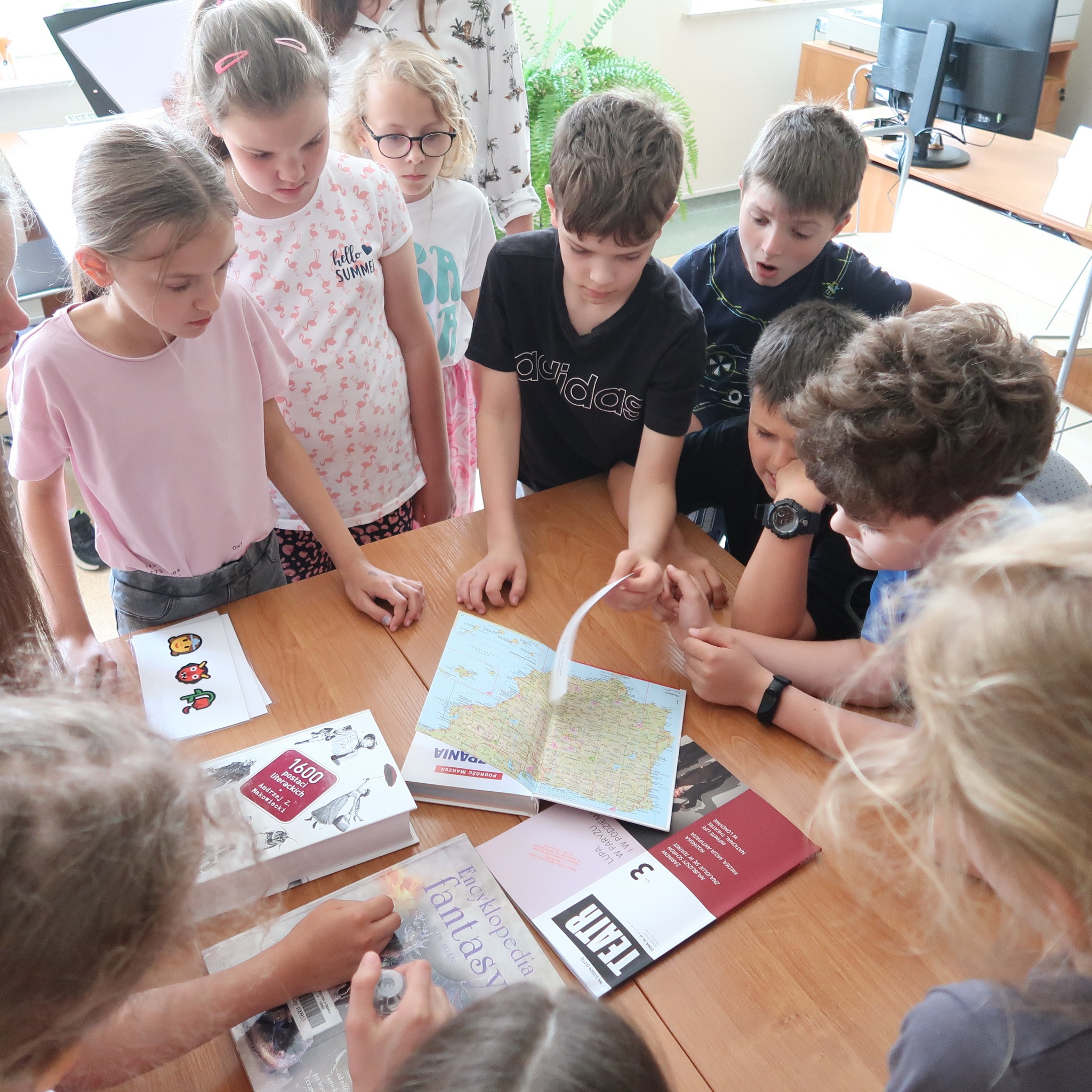 Grupa dzieci gromadzi się wokół stołu, na którym rozłożone są różne książki.