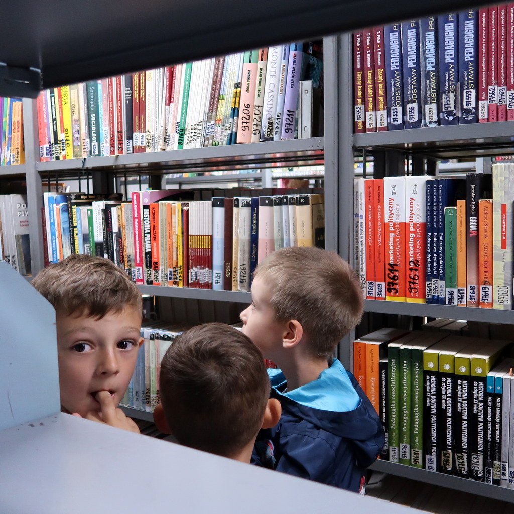 kolorowypotwor-1 Trzej mali chłopcy stoją miedzy regałami z książkami
