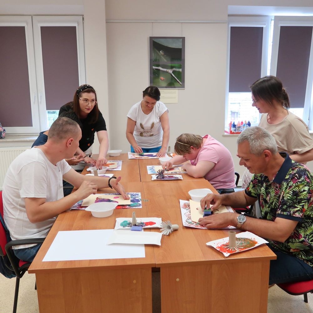 Uczestnicy warsztatów wykonują prace plastyczne siedząc przy stołach