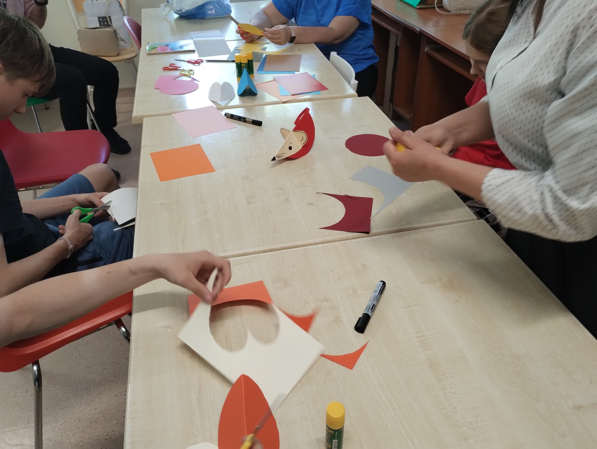 Grupa dzieci siedzących przy stole wykonuje zajmuje się wycinaniem myszek z papieru