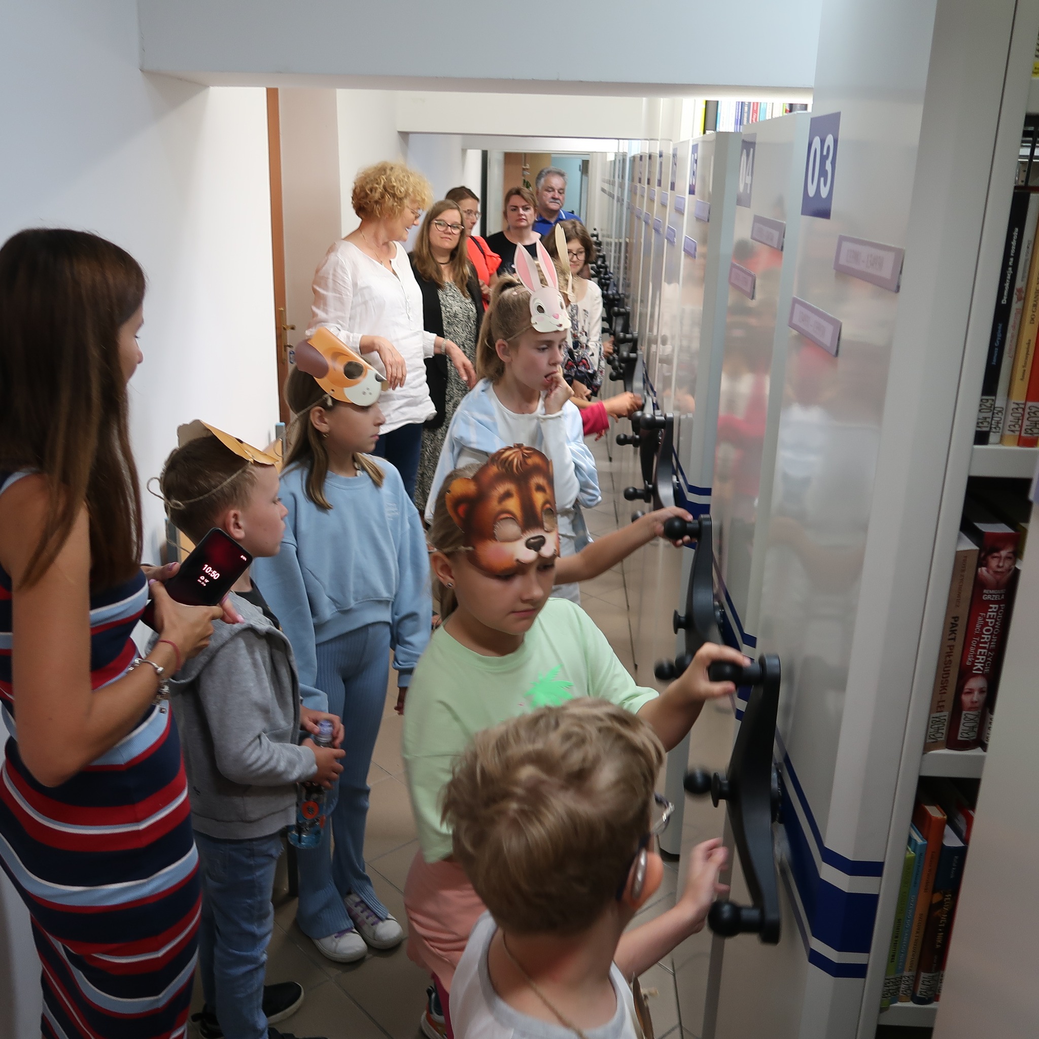 Dzieci z maskami zwierząt na twarzach zwiedzają magazyny biblioteczne z książkami