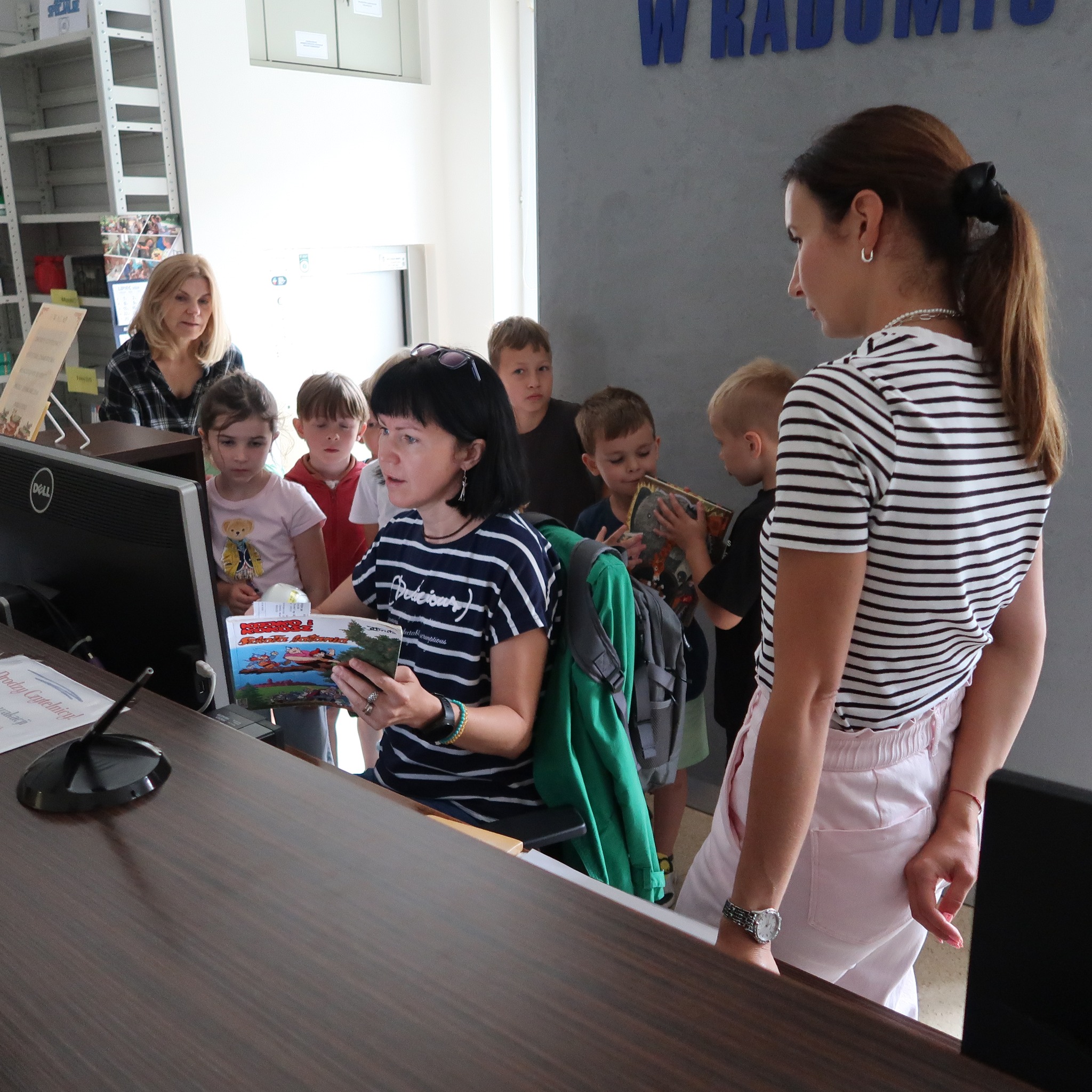 Bibliotekarka pokazuje dzieciom proces wypożyczenia książki w systemie