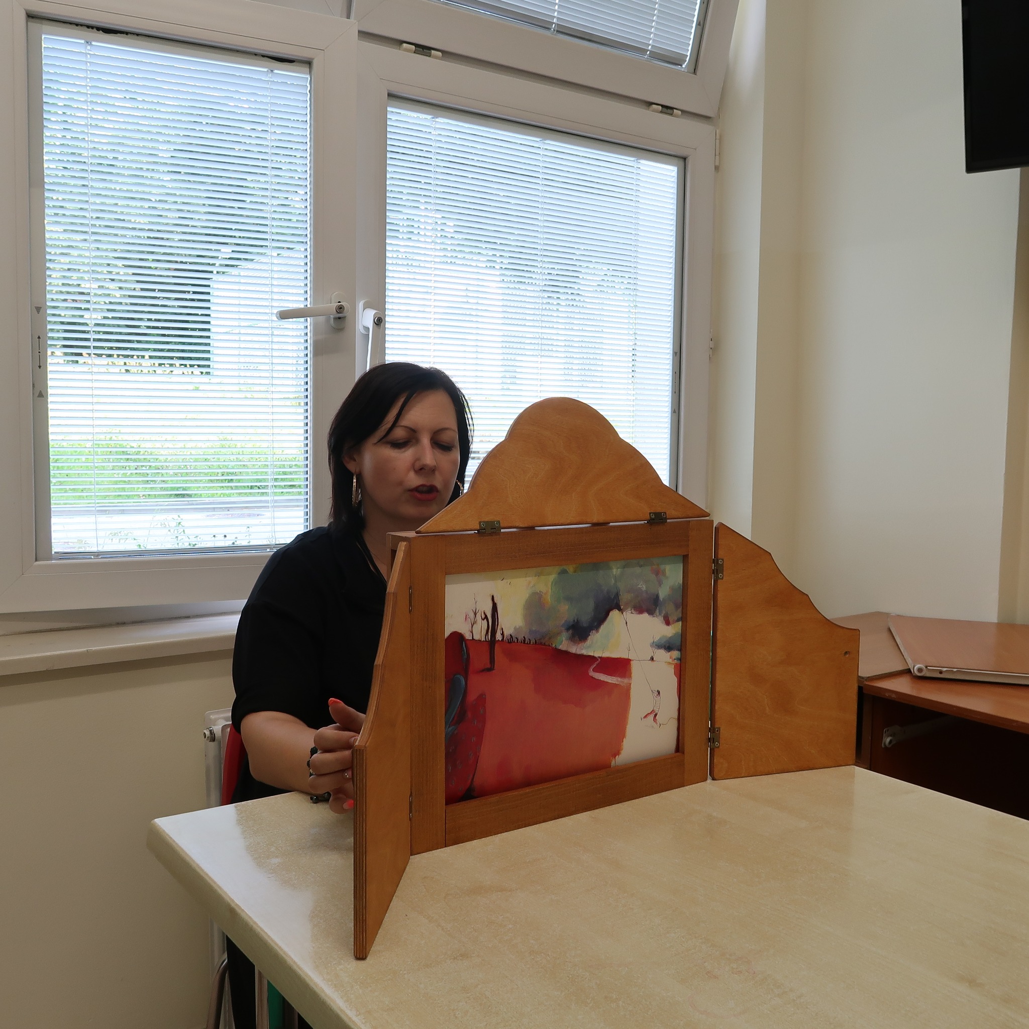 Pani prezentuje zebranym planszę teatrzyku kamishibai.