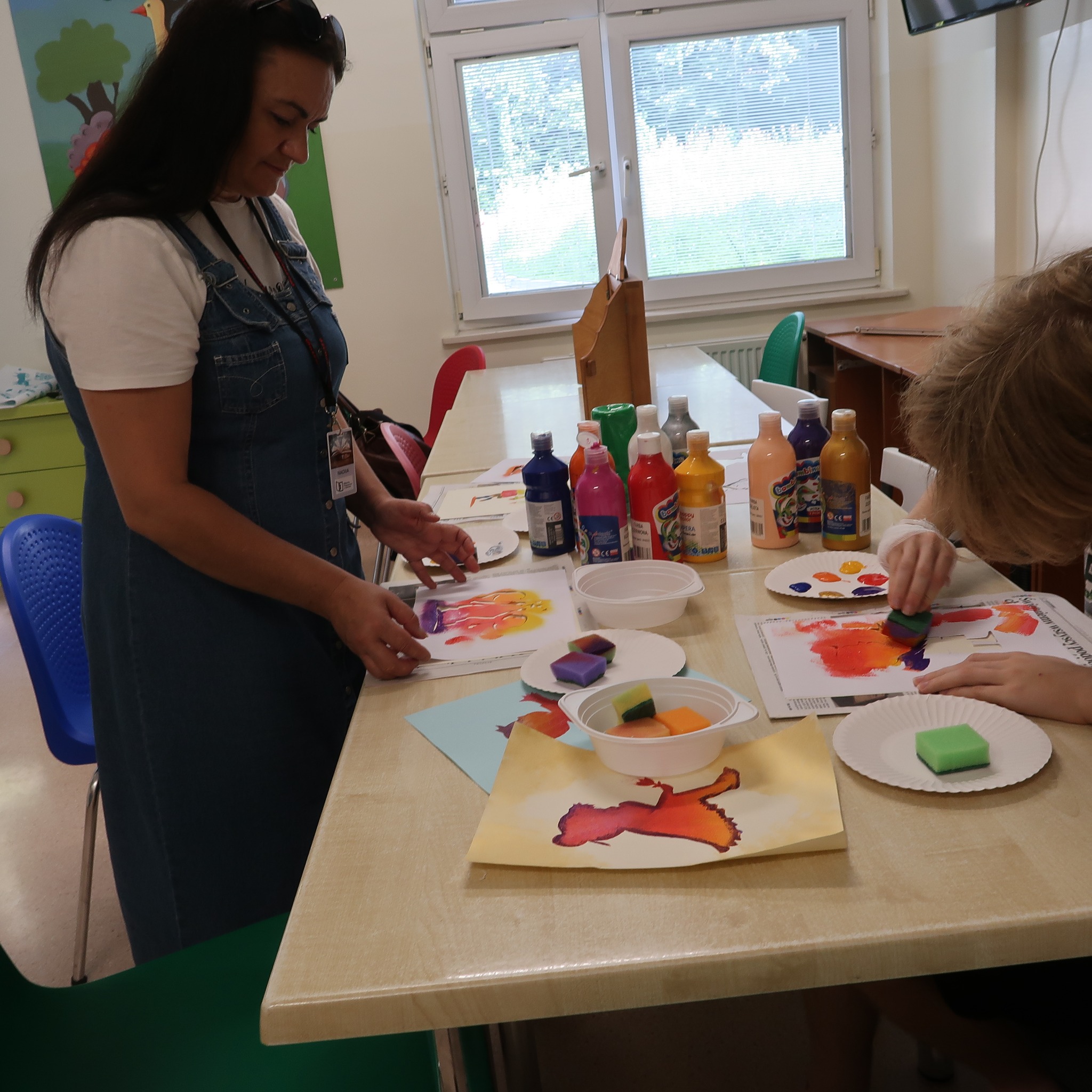 Pani prezentuje zebranym dzieciom techniki malarskie