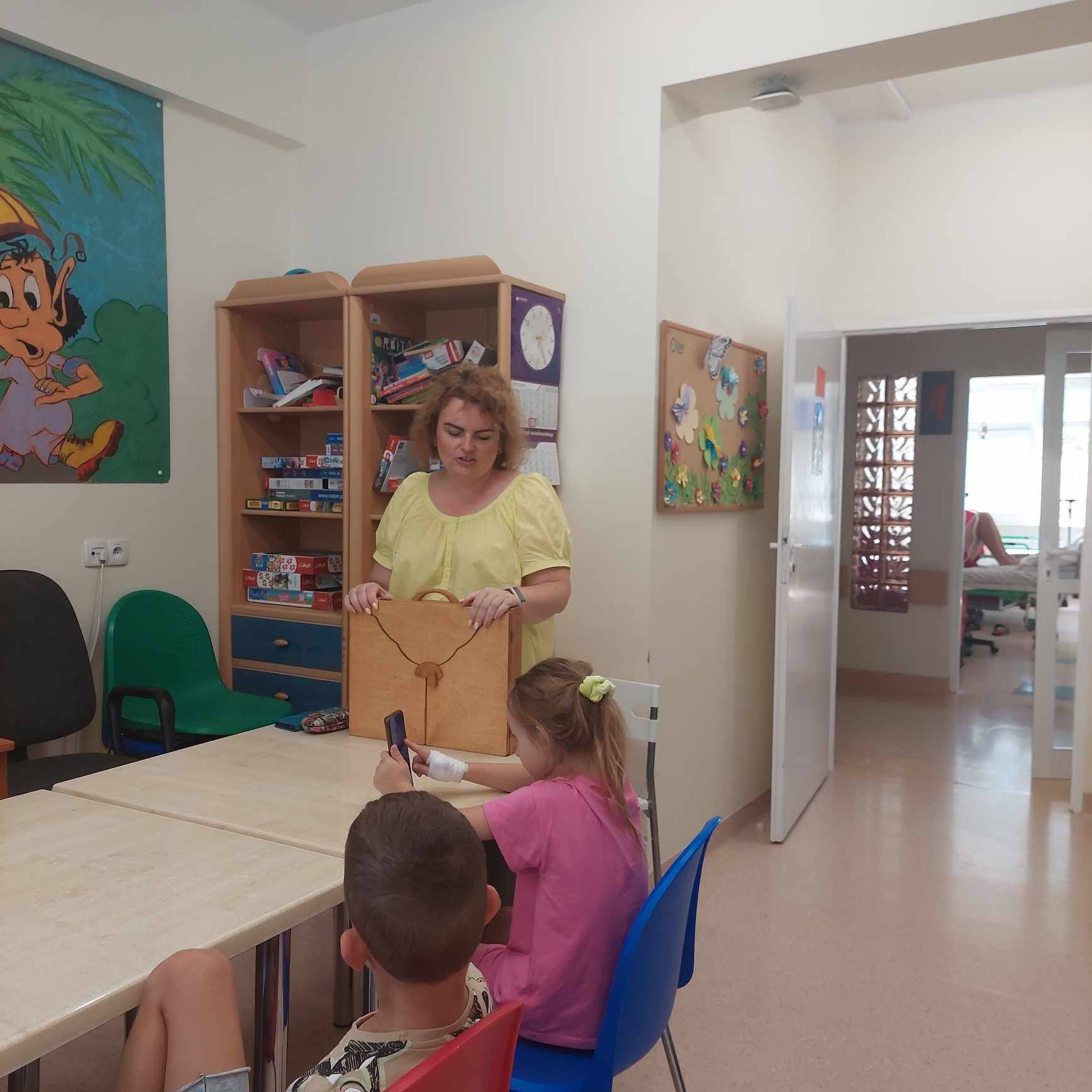 Kobieta stojąc prezentuje dzieciom teatrzyk kamishibai.