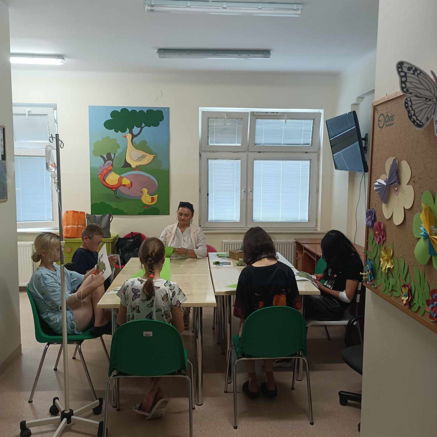 Dzieci siedząc przy stole wykonują prace plastyczne